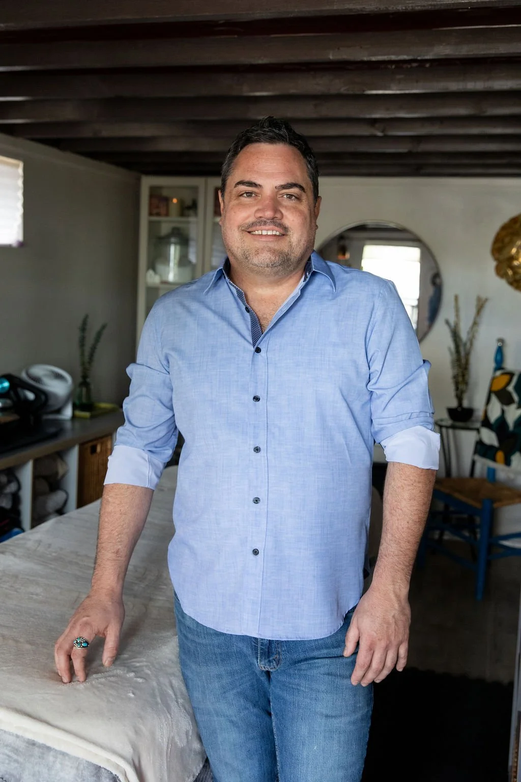 Chris Acosta, LMT and Board Certified Integrative Bodyworker, standing beside the massage table in his Fort Collins studio