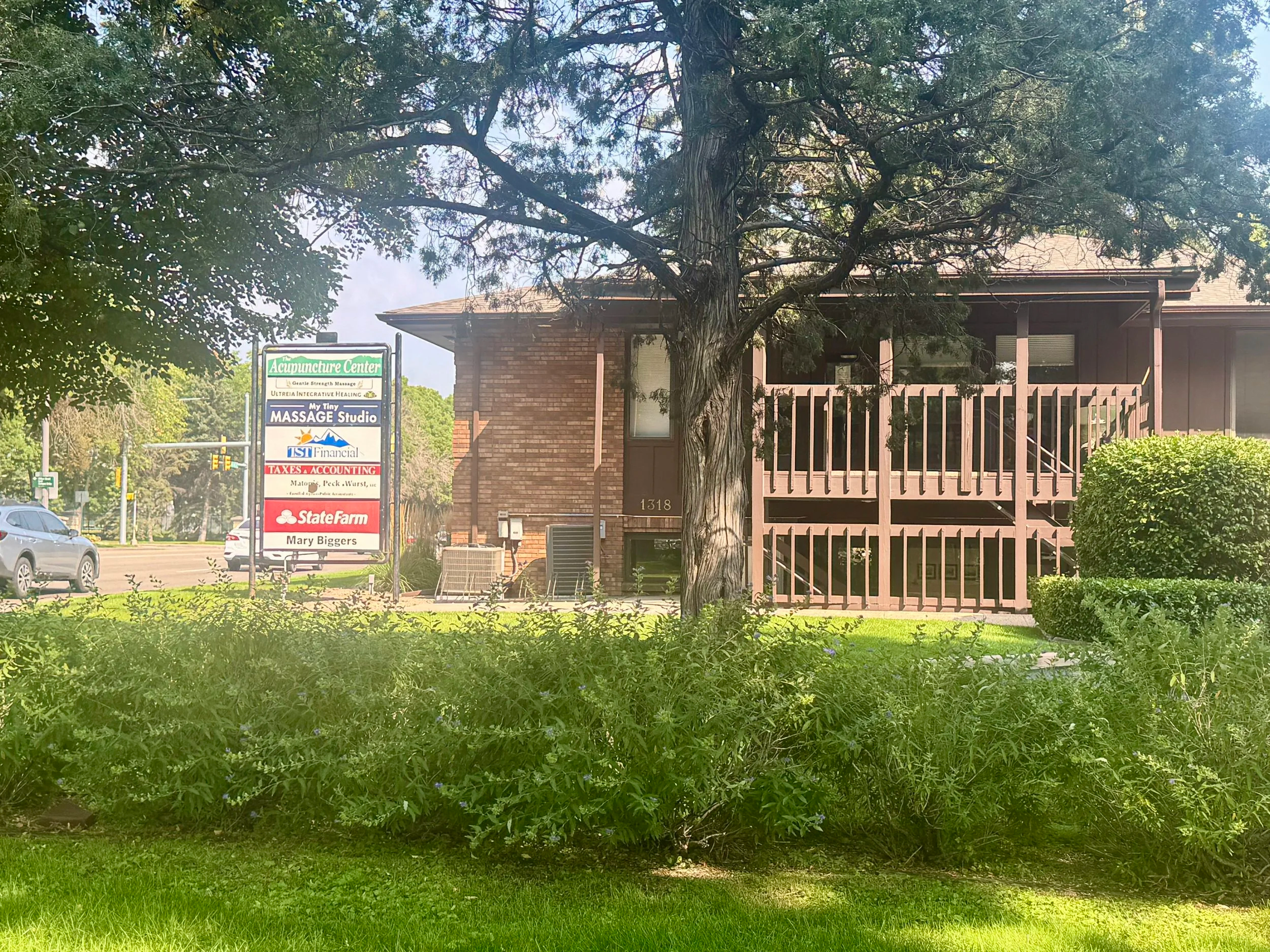Exterior of 1318 S. College Ave from the street — multi-tenant brown building with mature trees in foreground